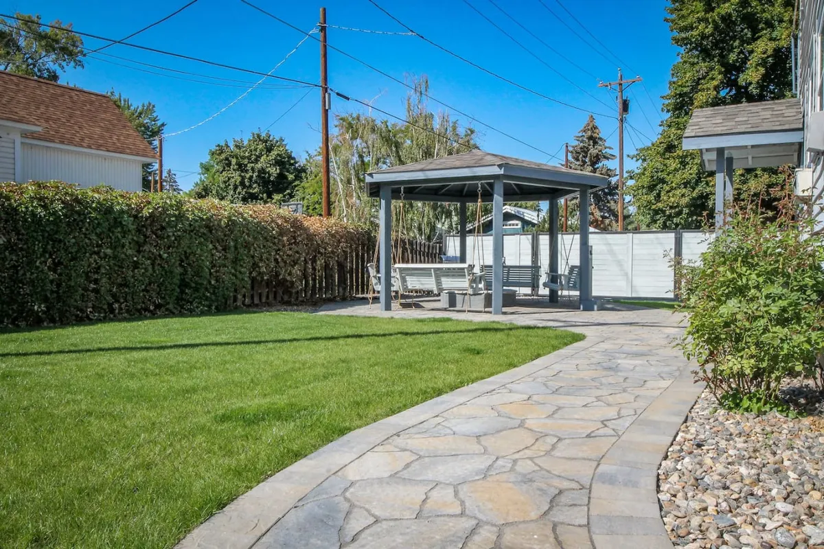 A peaceful garden scene with a gazebo, a stone pathway, and a lush green lawn. The gazebo is set up for outdoor dining, surrounded by natural beauty and perfect for relaxation after a day out.
