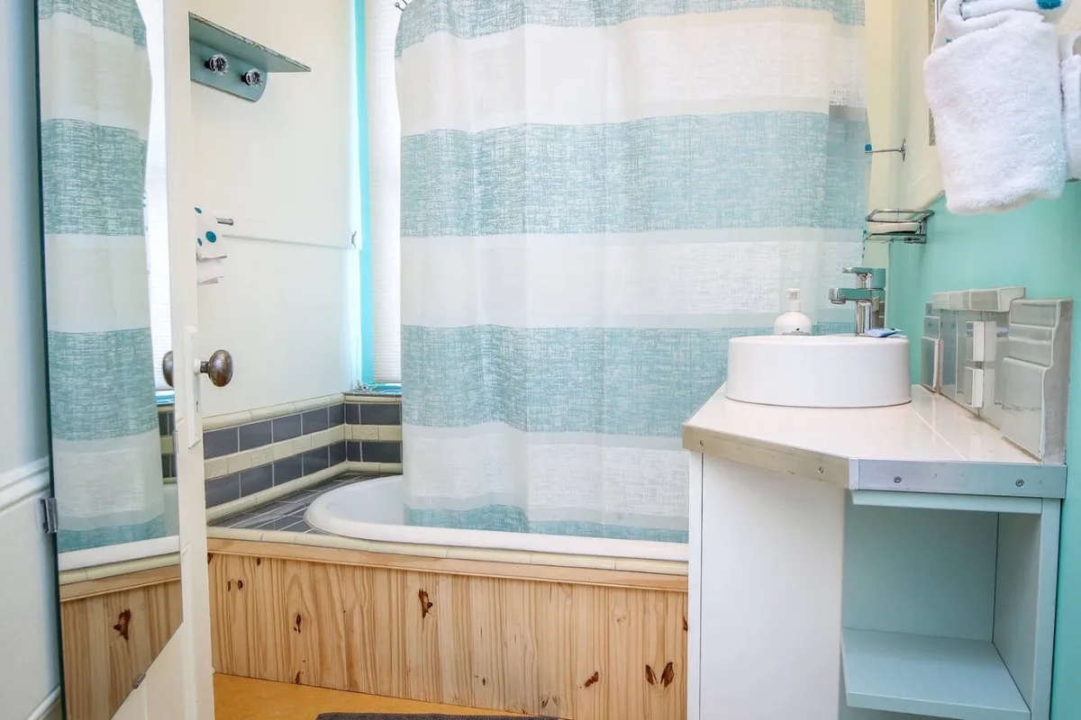 This image features a calm, serene bathroom scene showcasing a bathtub with a shower curtain and a sink in view. The setup radiates relaxation, providing a clear view of the soaking tub/shower combo, which is the centerpiece of the section. The clean, neutral tones and inviting ambiance evoke a sense of tranquility and comfort.