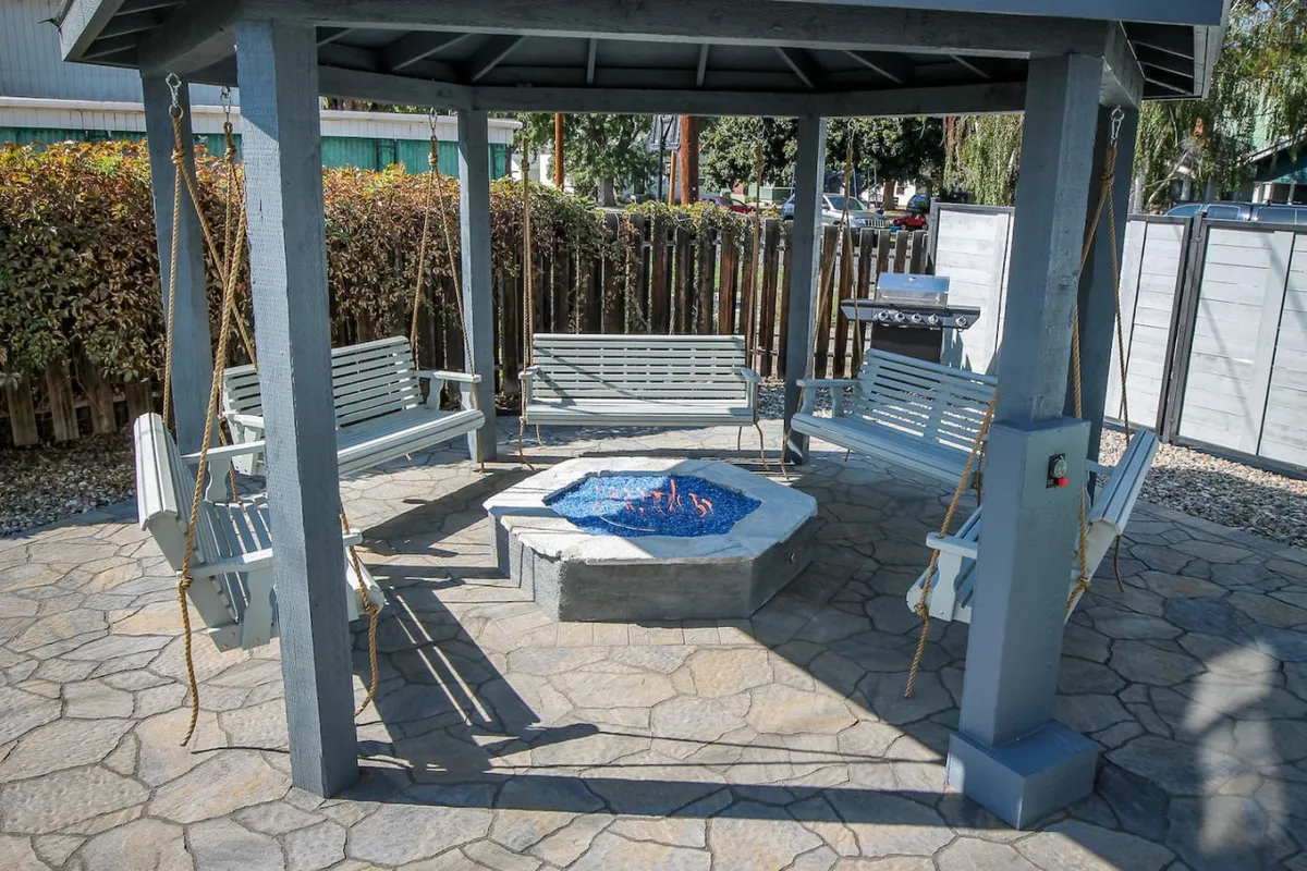 This image features an inviting outdoor area with a fire pit, cozy swing seats, and an overhead gazebo. The setting is designed for socializing and relaxing, providing an ambiance perfect for evening conversations or storytelling under the stars.