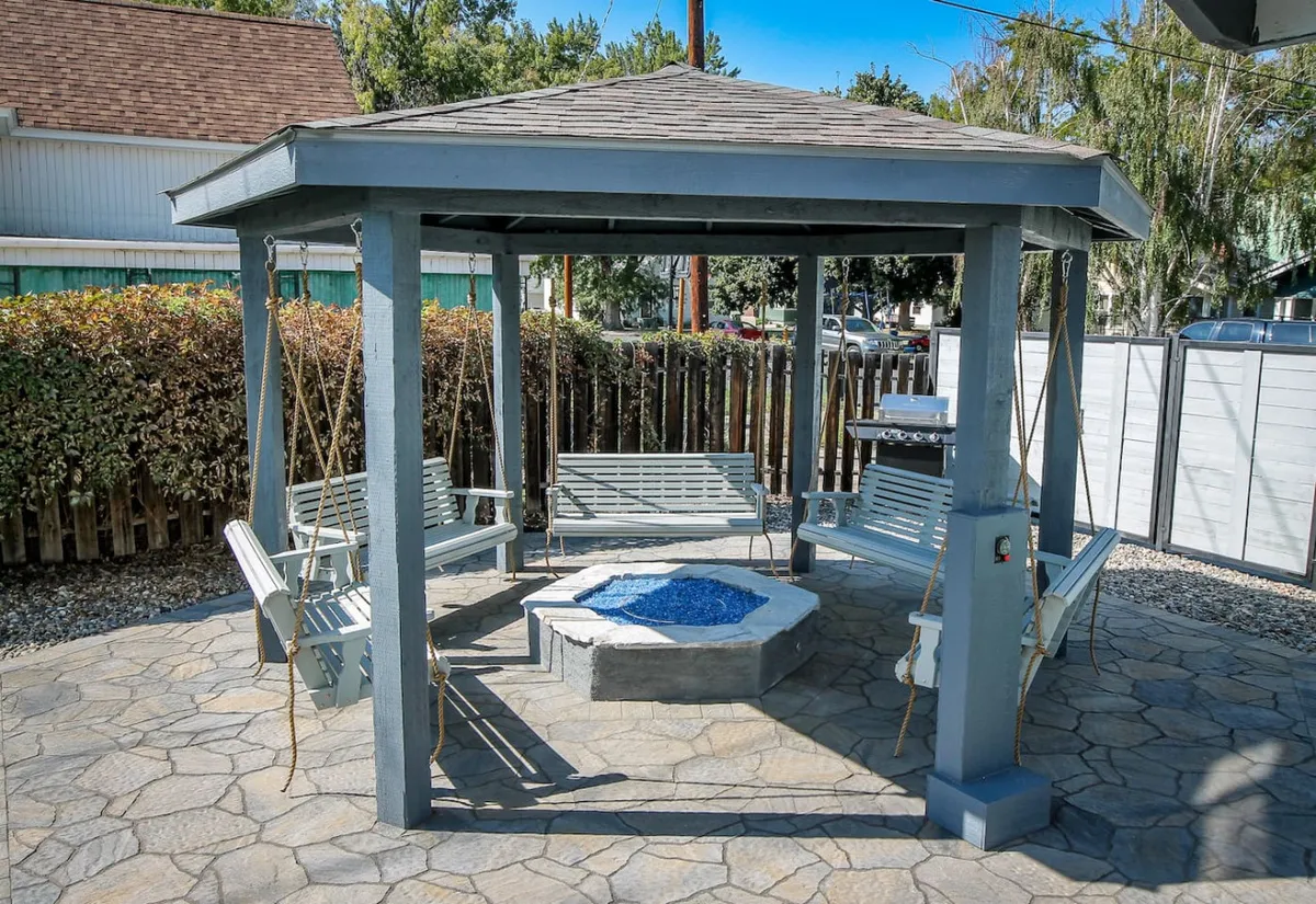 A broader view of the courtyard’s social space, highlighting multiple swings, a central fire pit, paved flooring, and surrounding greenery. The area is designed for relaxation and group gatherings, offering both openness and privacy.