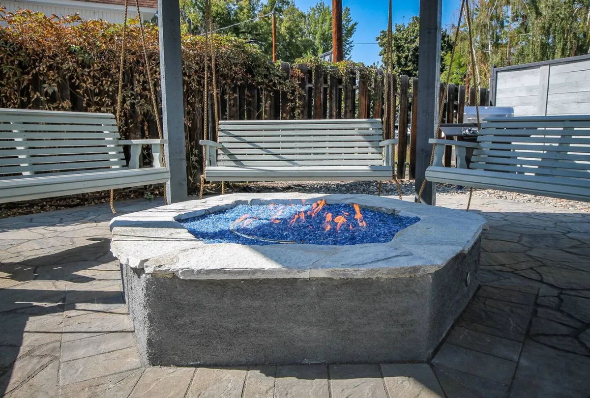 A tranquil scene showcasing swing benches arranged around a fire pit atop stone flooring. The comfortable seating and the warm glow of the fire create a cozy atmosphere ideal for both relaxation and social gatherings.