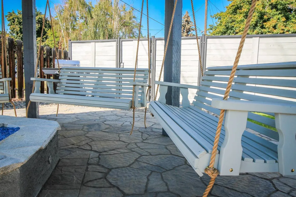 A tranquil outdoor gathering space featuring swing benches, a central fire pit, and stone flooring, all surrounded by greenery. The seating invites relaxation and social connection, while the open area suggests plenty of space for pets to enjoy alongside their owners.