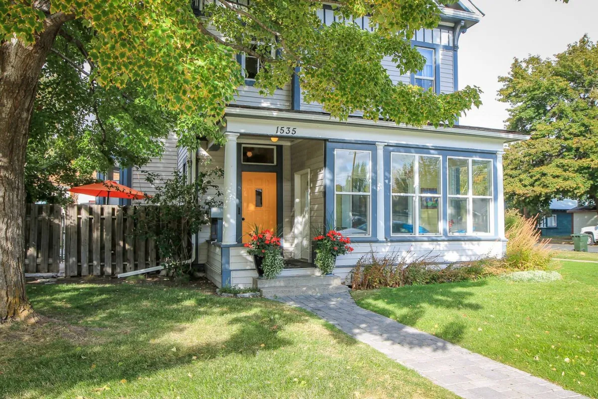 The inviting exterior of Palmer Four, featuring a welcoming front door, large windows, flower planters, and a well-kept pathway. The porch area shows people socializing and enjoying the garden, suggesting a friendly, accessible entryway for both humans and pets.