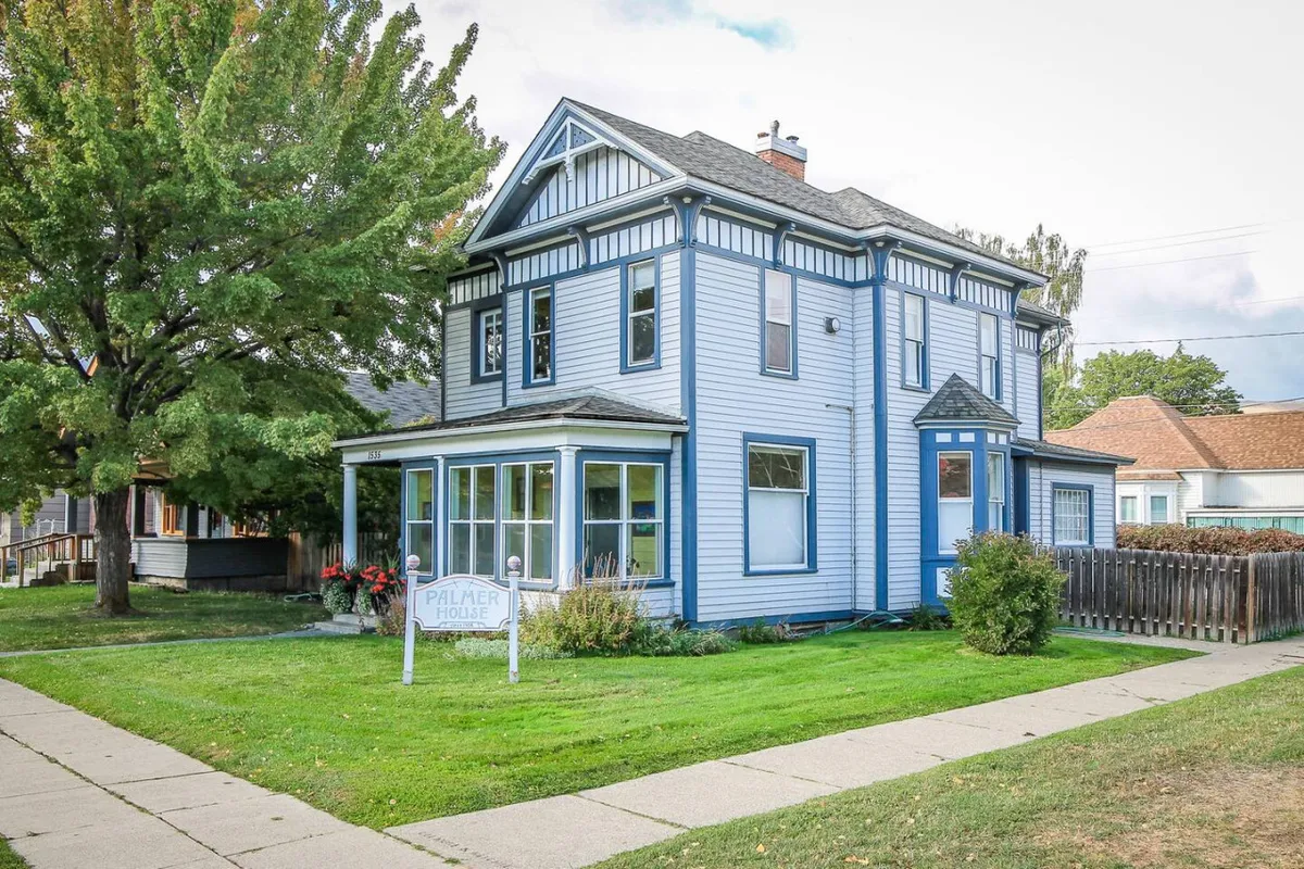 This image features the welcoming blue exterior of the house with large front windows and a charming front yard garden. The setting is bright and inviting, creating a sense of arrival and comfort.